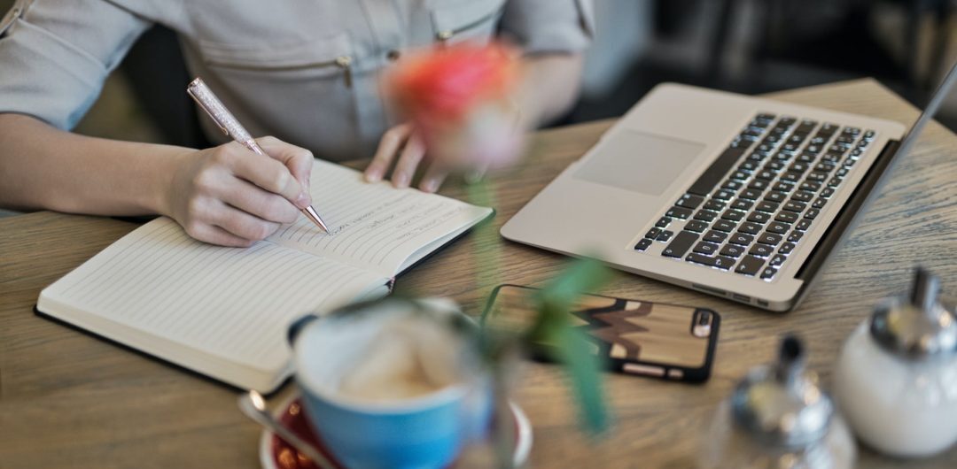 person writing on a notebook beside macbook