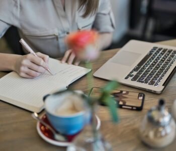 person writing on a notebook beside macbook