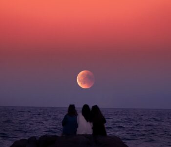 three women sitting on rock infront of ocean