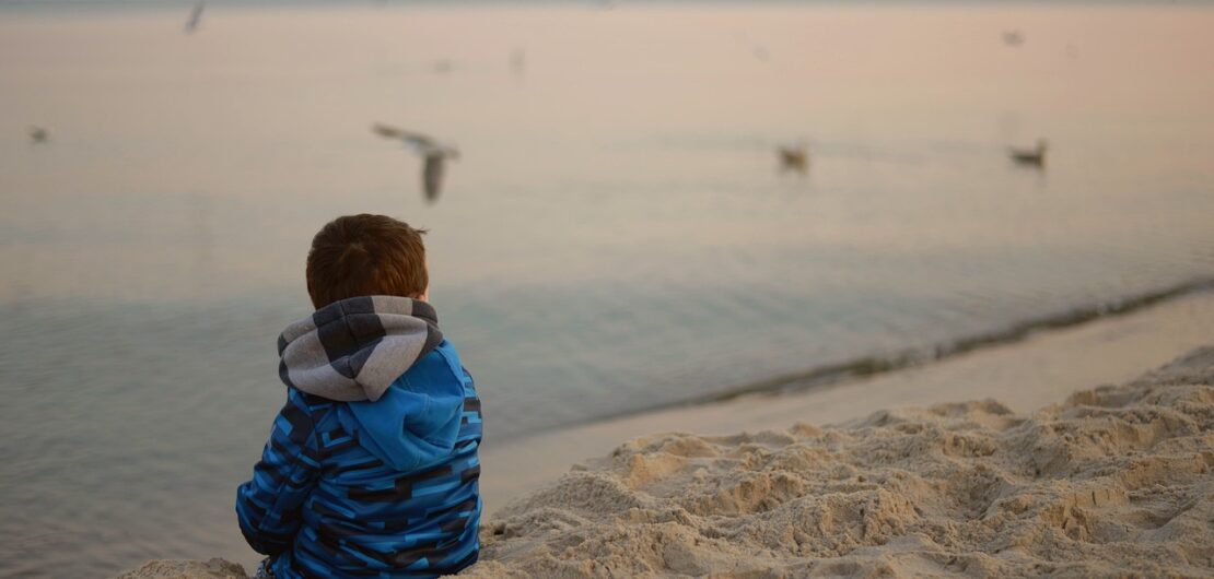 boy sitting alone looking out at the sea.