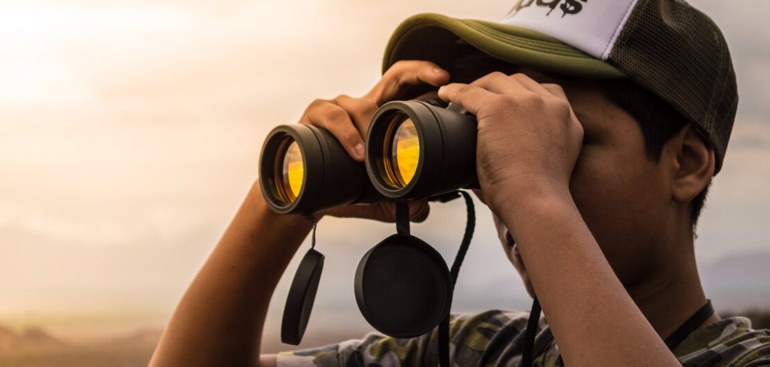 man looking in binoculars during sunset