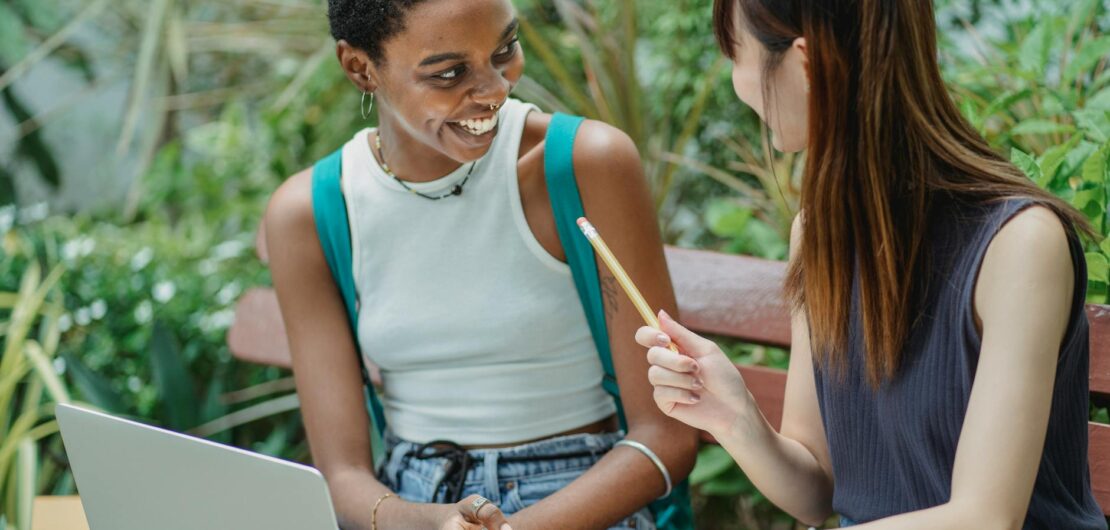 joyful multiethnic female students working on assignment in park