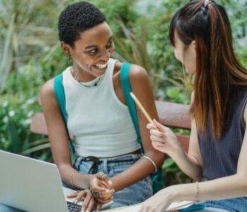 joyful multiethnic female students working on assignment in park