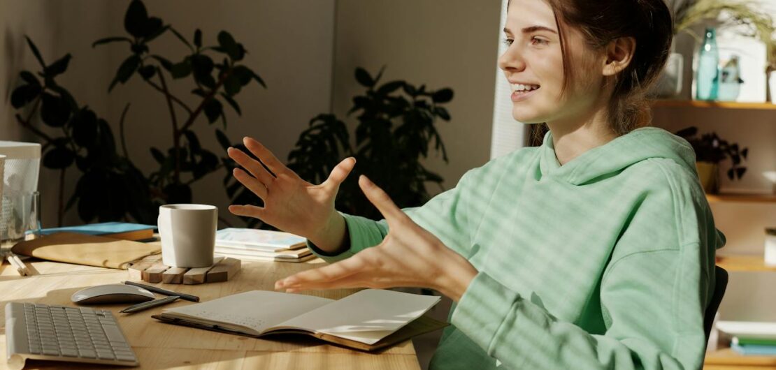 a woman in green hoodie sitting near the table while having conversation through her desktop