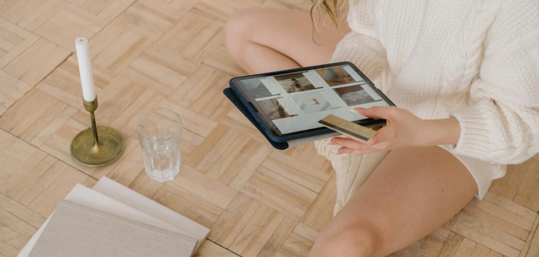Woman using a tablet for online shopping while sitting indoors with a bank card.